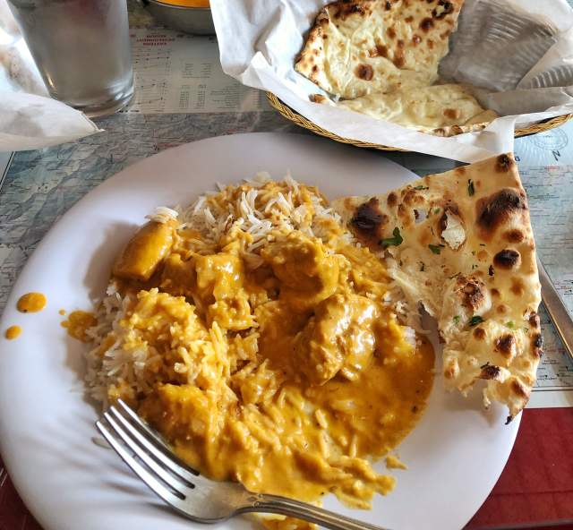 Butter chicken with basmati rice and naan sits on a table at Kathmandu Bistro, surrounded by additional curry dishes and freshly baked naan.