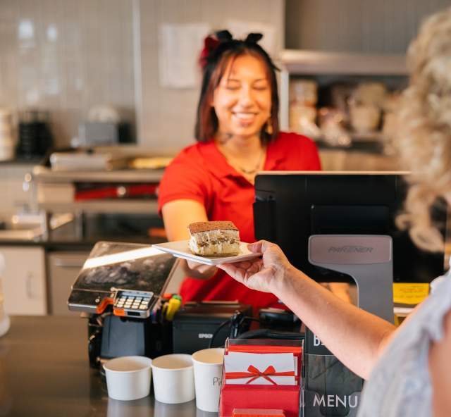 Woman behind the counter working at local lunch spot handing a desert to patron at The Bestro in Rapid City, SD.