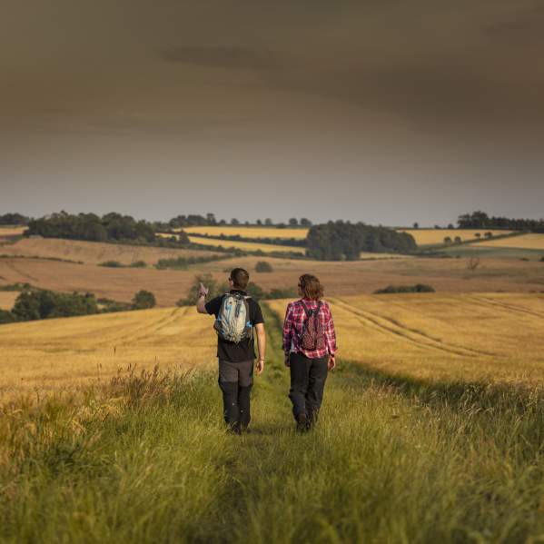 Two people walk away from the camera pointing into the distance. The background shows the Lincolnshire Wolds hills at sunset.