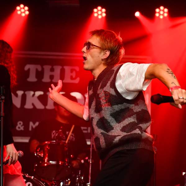 A male singer on a stage wearing sunglasses, holding a microphone, dancing