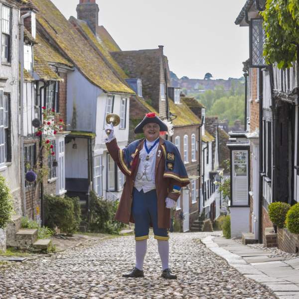 Rye cobbled street with Town Crier holding up his bell wearing traditional costume