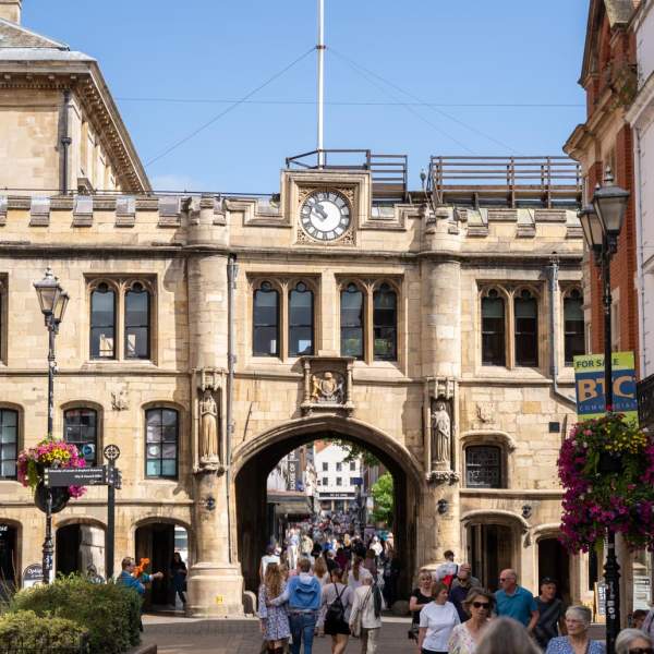 Lincoln Guildhall with people walking in the foreground and blue skies, with high street shops at the sides