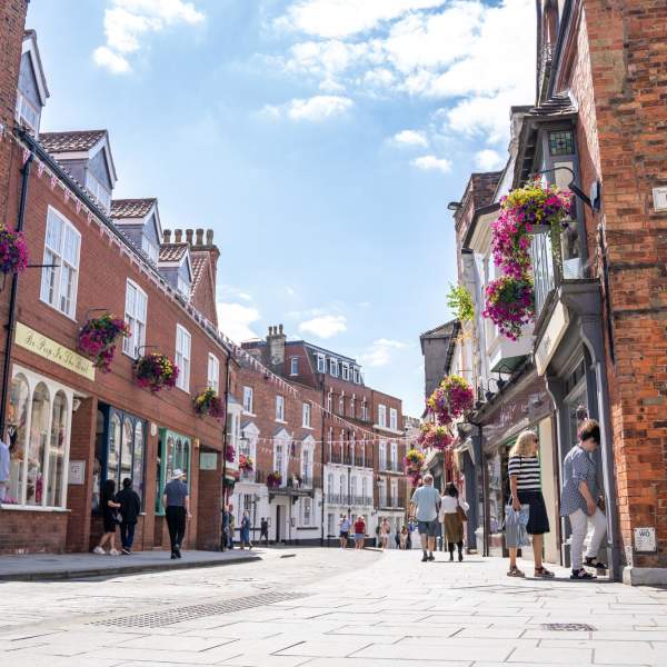 Lincoln's Bailgate street view with shopfronts and bunting on a sunny day with people shopping and walking along the pavement.