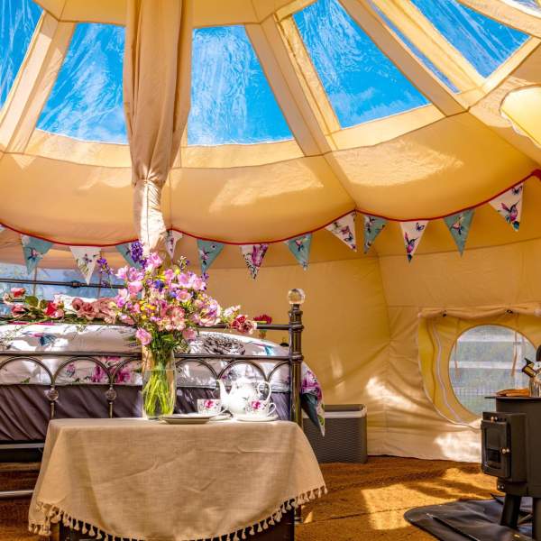 A glamping pod with woodburner and bed surrounded by flowers and bunting