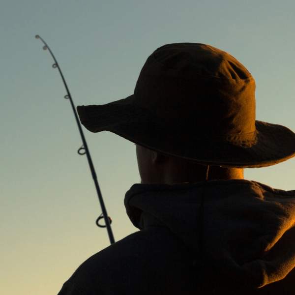 Photograph showing a person fishing from behind, with the dusk light only just illuminating them.