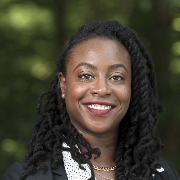 Woman with twisted black hair, smiling with a polkadot dress shirt and blazer.