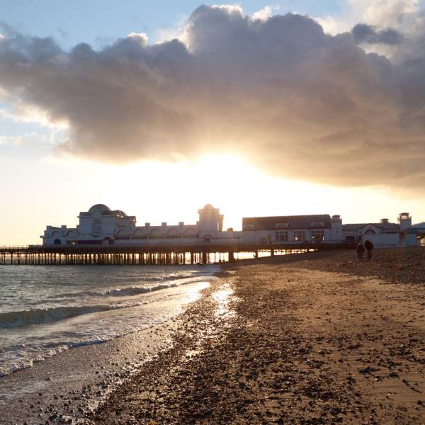 The sun sets behind South Parade Pier, with Southsea beach and sea in the foreground