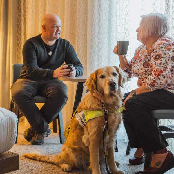 A couple relaxes in a modern hotel room at the DoubleTree by Hilton in Hull, sitting with a trained assistance dog beside them.