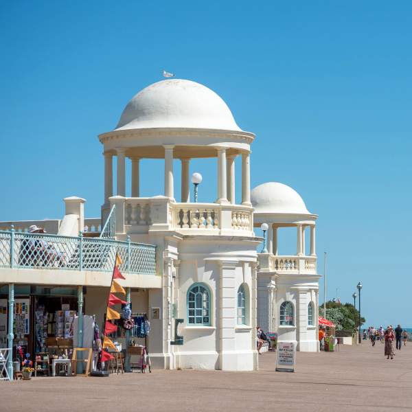 A sunny day in Bexhill on the promenade, with white cafe buildings and shops