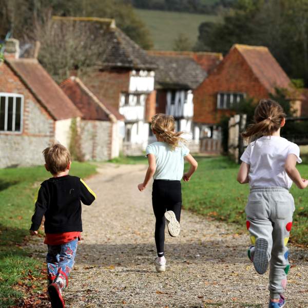 Three children run along the path towards the old buildings at Weald and Downland museum, Sussex