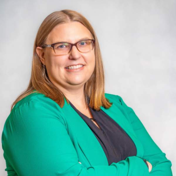 Woman wearing green blazer, smiling, brown glasses