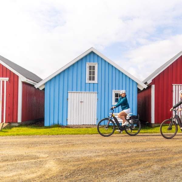 En mann og en kvinne på sykkel foran båthus i Farsund