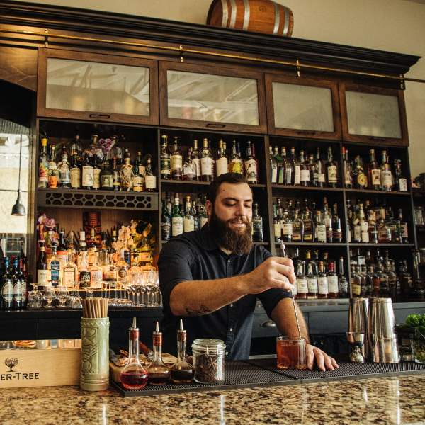A bartender crafting a cocktail at the well-stocked bar of The Ravenous Pig, with a warm, inviting atmosphere.