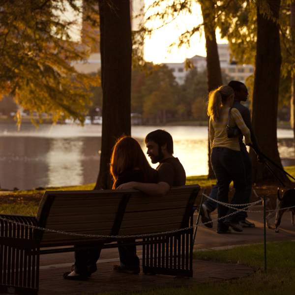 A couple sitting on a park bench and another couple walking their dog along Lake Eola