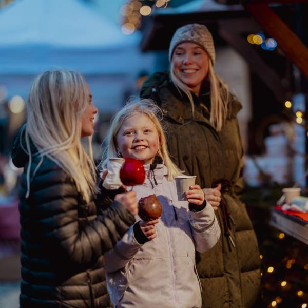 2 barn med godteri og 1 kvinne smiler ved julebodene i Kristiansand