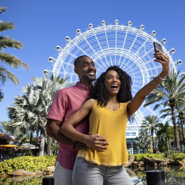 A couple posing for a selfie in front of The Wheel at ICON Park