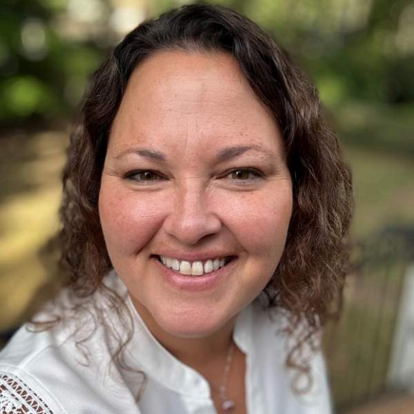 Selfie of woman with brown hair smiling, wearing a white blouse.
