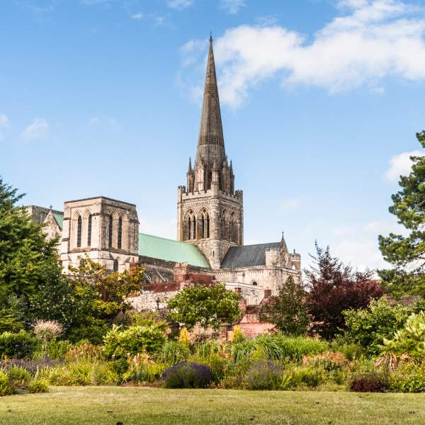 A view of Chichester Cathedral from the gardens with the spire reaching blue sky