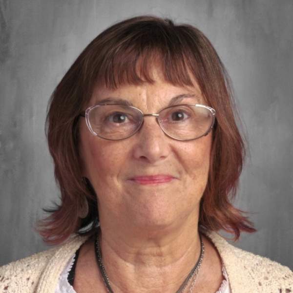 Woman wearing glasses and pink lip stick in a yellow cardigan.