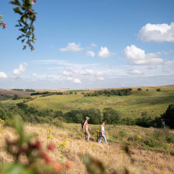 Two people walking along path on hillside with countryside in background and blue skies