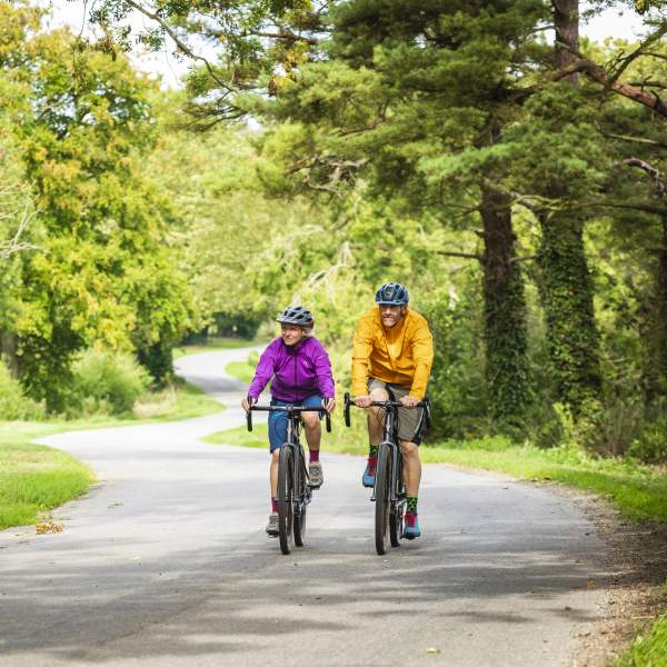 Two people cycling through a forest on a path