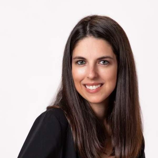 Professional Headshot of woman with dark brown hair, smiling, wearing a black longsleeve blouse.