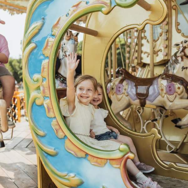 two girls on a brightly coloured carousel waving at passers by