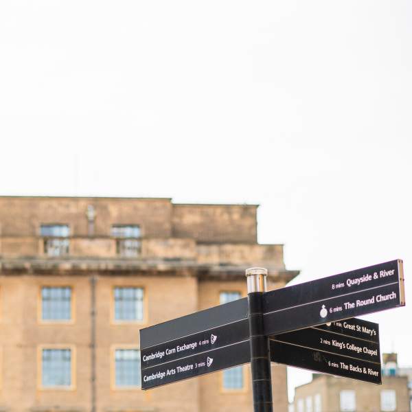 A Cambridge signpost on the bottom right corner with an old yellow building blurred in the background