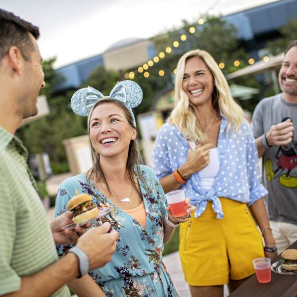 Four friends smiling an chatting while sampling food and drink items at EPCOT