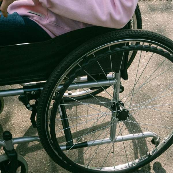 Photograph of a wheelchair user in a pink hoodie, sat in their chair