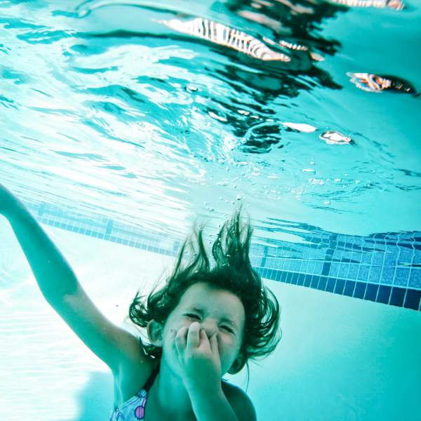 Jente som holder seg for nesen under vann i et svømmebasseng. Foto.