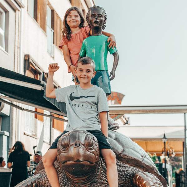 To barn som sitter på skulpturen Gutten og skilpadden i gågata i Sarpsborg. Foto.
