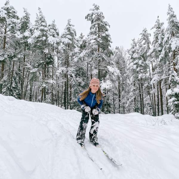 Barn som står på ski ned en bakke i skogen. Foto.