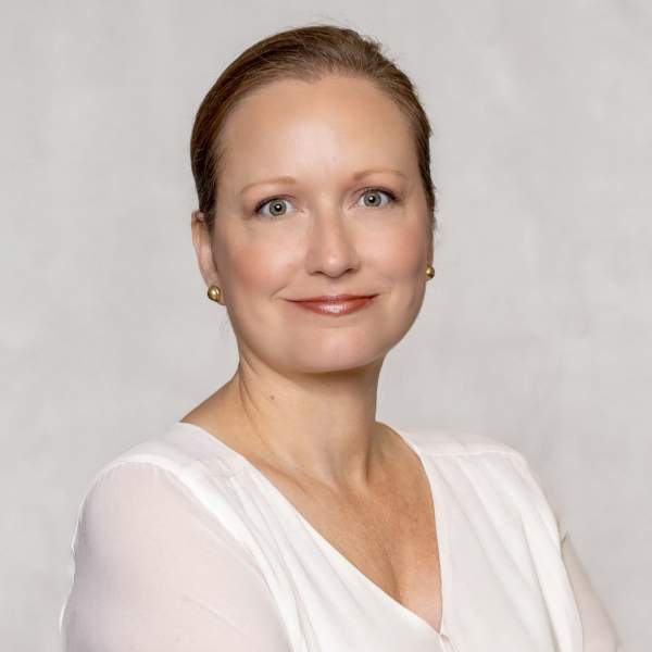 Professional headshot of woman with hair pulled back, smiling, wearing a white blouse.