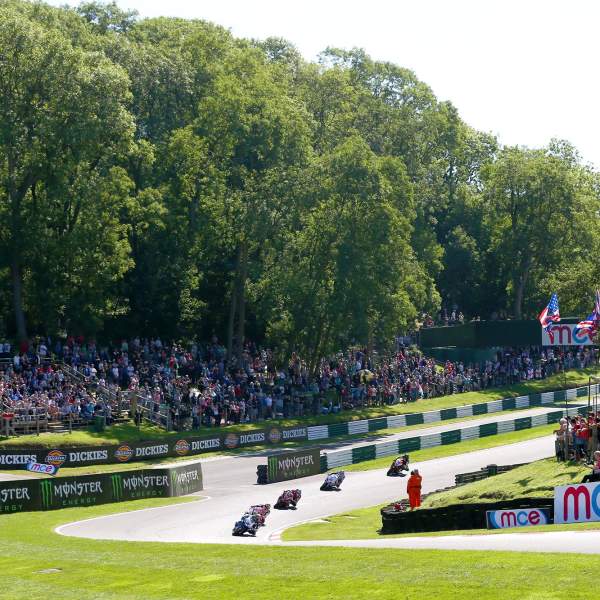 A race track with motorbikes and audience stood around on grass banks