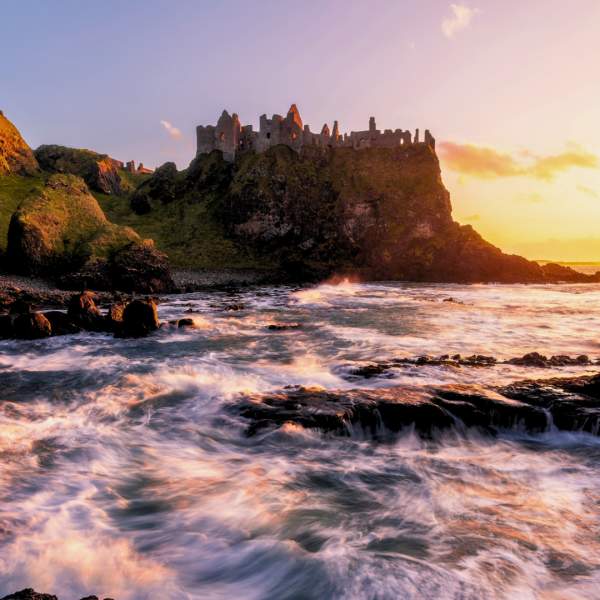 Dunluce Castle perched on dramatic coastal cliffs at sunset in autumn, overlooking the Atlantic Ocean on Northern Ireland's Causeway Coast