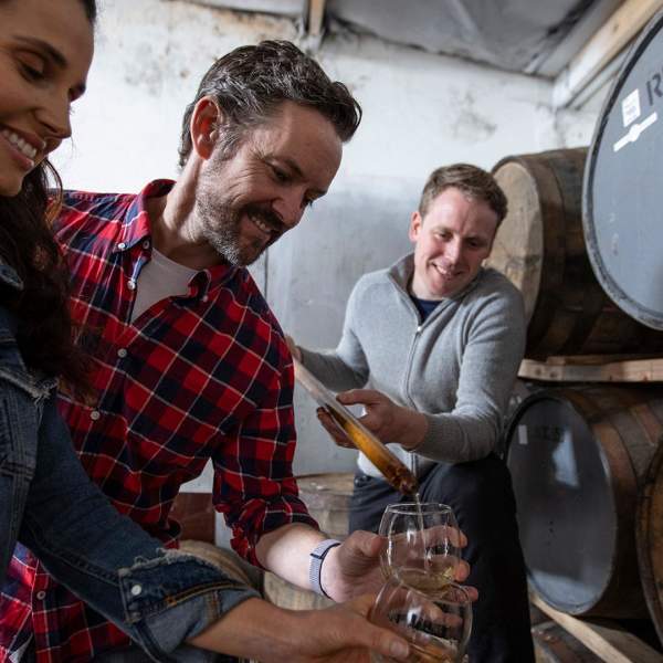 Couple enjoying a tour at Killowen Distillery while the guide pours liquid into their glasses for sampling