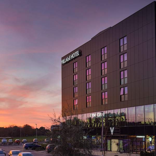 Photograph showing a Village Hotel at dusk, with the sun setting and creating a purple and orange-hued sky