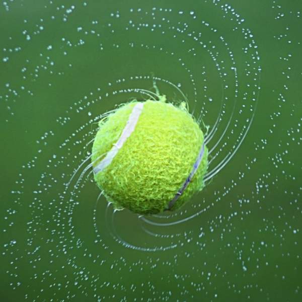 Photograph showing a spinning wet tennis ball, with water droplets flying off it
