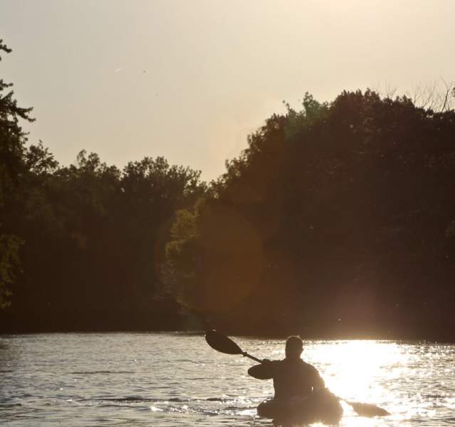 Kayaker paddling the Kankakee river, silhouetted by the sun