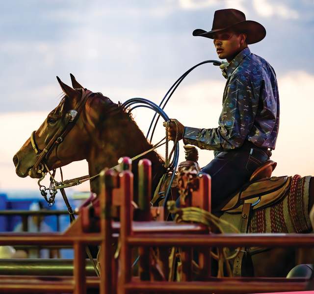 A cowboy rodeo participant sits on his horse with his rope at the ready
