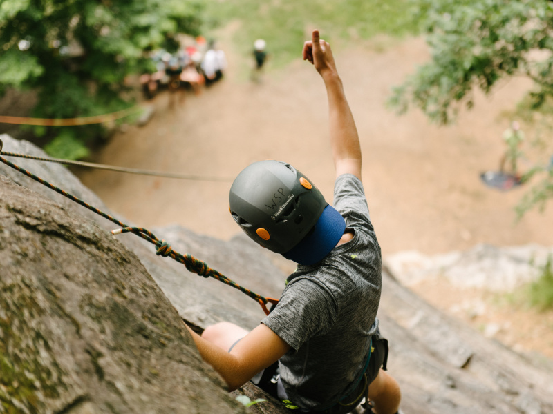 Man rock climbing on a cliff giving a thumbs up