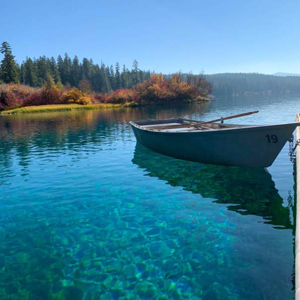A drift boat sits on clear turquoise waters with fall foliage on the banks.