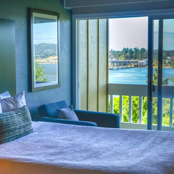 A hotel room bed with a balcony view of the Siuslaw Bay.