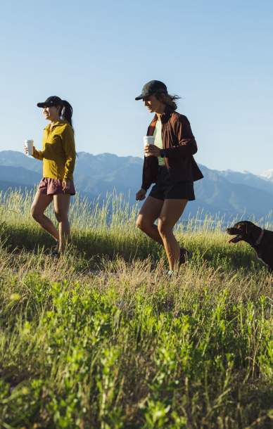 Three girls and a dog hiking on a trail through green grass with mountains in the background