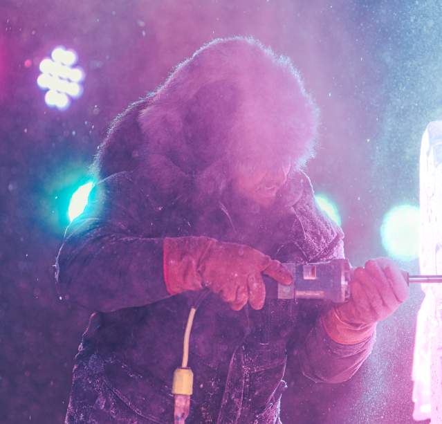An ice carver using a power tool to carve a sculpture during the Freezefest ice battle