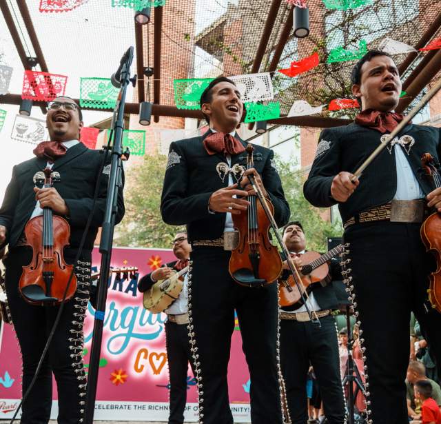 Mariachis standing in front of papel picado