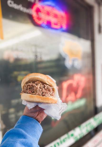 hand holding a large pulled pork sandwich
