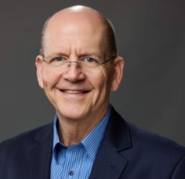 Scott Blalock wearing a blazer smiling into the camera posing for a headshot.
