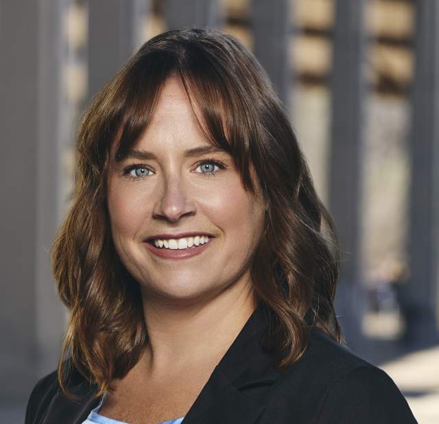 A woman wearing a black blazer smiling into the camera for a headshot.